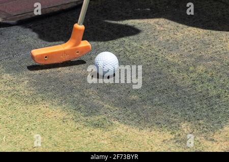 Gros plan d'une mini-balle de golf et d'un mini-putter orange sur gazon artificiel en plein air avec espace de copie. Banque D'Images