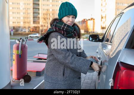 Femme caucasienne ouverture bouchon couvercle de réservoir de voiture sur station-service, hiver saison, femme regardant la caméra, hiver saison Banque D'Images