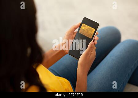 Femme utilisant le téléphone tout en étant assise sur la table, payant avec le toucher Banque D'Images