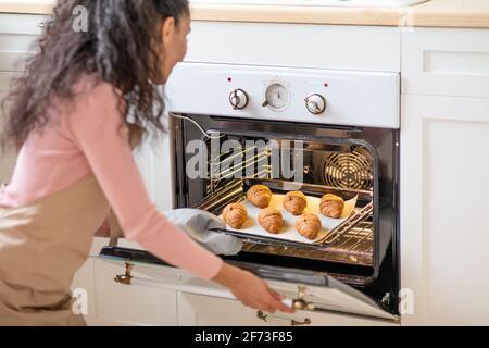 Une jeune femme méconnaissable prend un plateau avec des croissants au four Sur la cuisine Banque D'Images