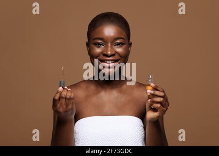 Huiles essentielles pour le soin de la peau. Belle femme noire tenant une bouteille avec le sérum de visage Banque D'Images