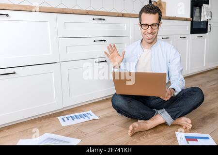 Un homme d'affaires heureux et prospère utilise un ordinateur portable, fait signe à ses collègues lors d'une réunion vidéo, sourit. Homme indépendant élégant ayant une conférence en ligne Banque D'Images