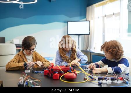 Vue de face portrait de trois enfants mignons construisant des robots pendant la classe d'ingénierie dans l'école de développement, l'espace de copie Banque D'Images