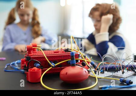 Gros plan de la machine robotique rouge sur la table en classe d'ingénierie avec les enfants en arrière-plan, espace de copie Banque D'Images