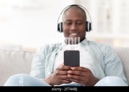Application lecteur de musique pour smartphone. Homme afro-américain qui écoute du son sur un téléphone portable et qui porte un casque sans fil Banque D'Images