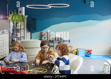 Portrait grand angle de trois enfants mignons construisant des robots pendant la classe d'ingénierie dans l'école de développement, l'espace de copie Banque D'Images