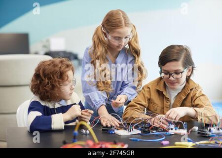 Vue de face de trois enfants construisant des robots pendant l'ingénierie classe dans l'école de développement Banque D'Images