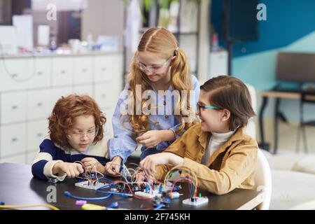 Portrait de trois enfants souriants expérimentant avec des circuits électriques pendant construction de robots en cours d'ingénierie à l'école Banque D'Images