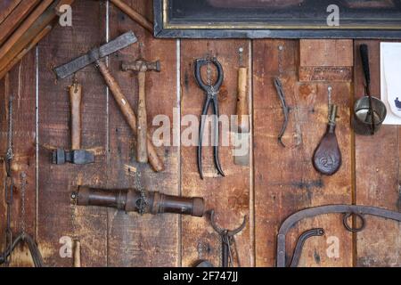 Rustique vieux outils de ferme en métal antique comprenant un marteau, une pince en fer, une tasse, et des objets artisanaux rouillés accrochés à un vieux mur de hangar de grange en bois Banque D'Images