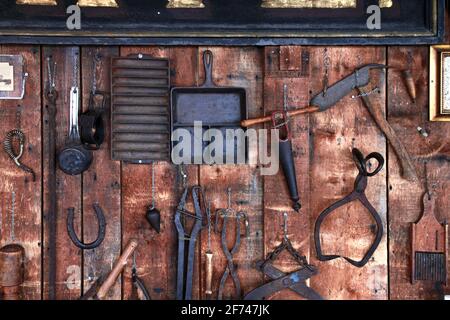 Outils en métal ancien rustique, pince, griffe à col rugueux, pince, tasse en métal, fer à cheval, articles artisanaux suspendus sur un mur de hangar de grange en bois ancien Banque D'Images