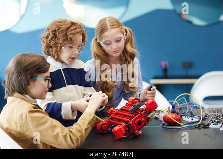 Portrait de trois enfants mignons construisant le robot ensemble tout en appréciant classe d'ingénierie dans l'école de développement Banque D'Images