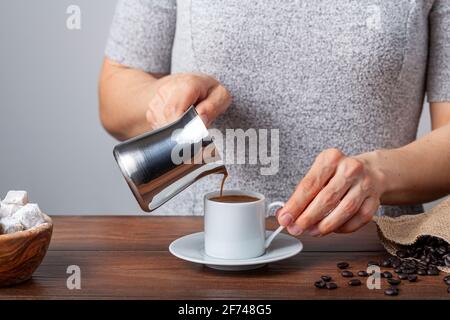 Café turc traditionnel servi dans des tasses classiques avec des délices turcs. Une cafetière métallique est en arrière-plan. Une femme verse du café au c Banque D'Images