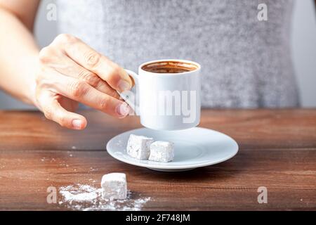 Une femme turque de race blanche boit du café turc traditionnel dans une tasse spéciale. Le café est servi avec un délice turc sur le côté de l'assiette Banque D'Images