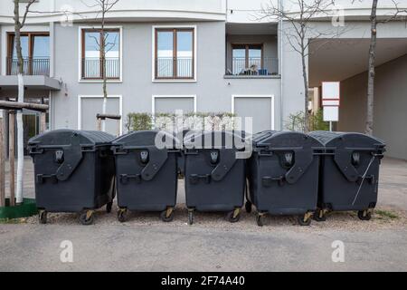 Vue de l'extérieur et de la mise au point sélective sur un groupe de poubelles en plastique noir sur le trottoir et le fond du bâtiment résidentiel en Europe. Banque D'Images