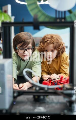 Vue avant portrait de deux écoliers regardant l'imprimante 3D pendant les cours d'ingénierie à l'école moderne, espace de copie Banque D'Images