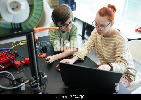 Vue en grand angle chez une jeune femme enseignant aidant le garçon à utiliser Imprimante 3D pendant les cours de robotique et d'ingénierie à l'école Banque D'Images