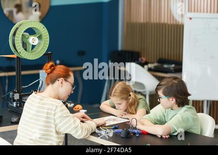 Portrait de deux enfants adorables à l'écoute d'une enseignante pendant les cours d'ingénierie et de robotique à l'école moderne, espace de copie Banque D'Images