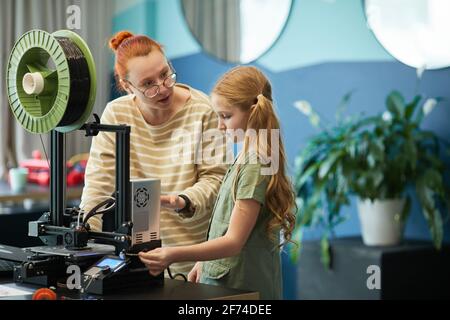 Portrait d'une enseignante aidant une jolie fille à utiliser une imprimante 3D pendant les cours d'ingénierie et de robotique à l'école moderne, espace de copie Banque D'Images