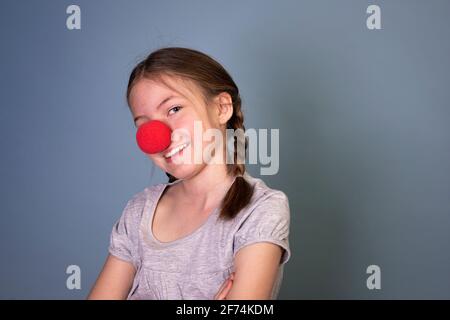 jolie jeune fille au nez clown rouge et deux tresses et chemise grise sur fond bleu Banque D'Images