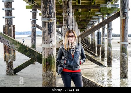 Tendance, bien habillée décontractée femme d'âge moyen souriant dans l'appareil photo et debout sous le plus long quai du Canada, le White Rock Pie, d'une longueur de 470 mètres Banque D'Images