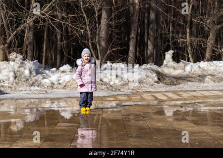 bonne fille sautant sur les flaques du printemps et riant Banque D'Images