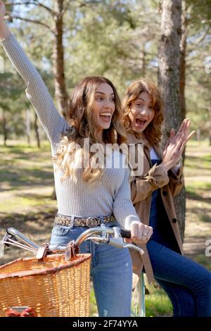 De jeunes amies souriantes et souriantes regardent l'appareil photo à vélo dans un parc ensoleillé en été Banque D'Images