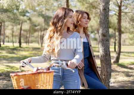 De jeunes amies souriantes et souriantes regardent loin à vélo parc ensoleillé en été Banque D'Images
