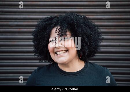 Contenu adulte en surpoids femme cheveux bouclés contre le mur côtelé dedans jour et regarder la caméra Banque D'Images