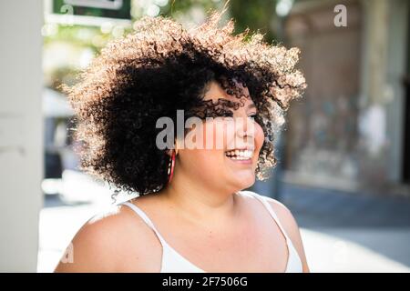 Femme adulte souriante avec une coiffure afro qui regarde loin ville éclairée à l'arrière Banque D'Images