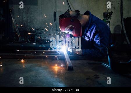 Travailleur sans visage en gants et en métal de soudage uniforme sur la table près des constructions en usine Banque D'Images