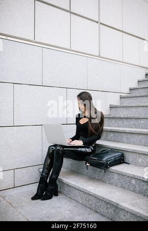 Vue latérale d'une femme entrepreneur concentrée assise sur des marches en pierre en ville et en naviguant sur netbook tout en travaillant sur le projet en ligne Banque D'Images