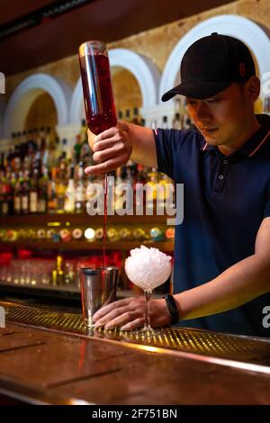 Jeune barman asiatique versant du jus de fraise dans le shaker pendant préparation d'un cocktail au bar Banque D'Images