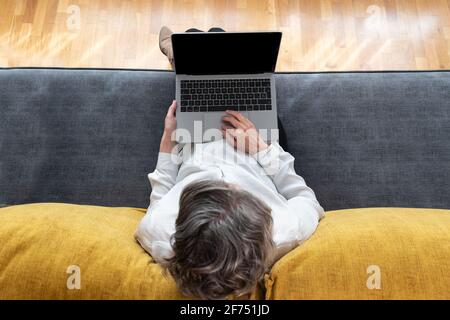 Vue de dessus de l'anonyme femme travailleur à distance surfant sur Internet netbook sur un canapé à la maison Banque D'Images