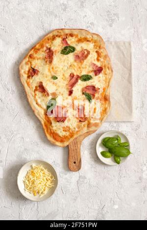 Au-dessus de savoureuses pizzas faites maison avec du basilic et du jambon servi sur une planche à découper en bois sur table Banque D'Images