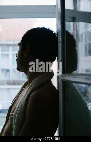 Vue latérale d'un homme pensif assis sur le rebord de la fenêtre à la maison Banque D'Images
