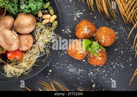 Vue de dessus de savoureuses croquettes frites avec de la poudre d'ail et des feuilles d'herbes fraîches près de l'assiette avec des légumes variés Banque D'Images