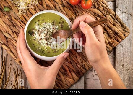 Vue de dessus de la récolte cuisson non reconnaissable avec une cuillère en bois et bol de soupe crémeuse appétissante aux pistaches écrasées et aux épices Banque D'Images