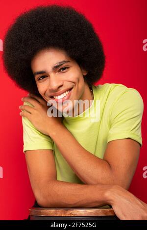 Jeune homme afro-américain auto-gai dans un t-shirt décontracté regarder l'appareil photo sur fond rouge Banque D'Images