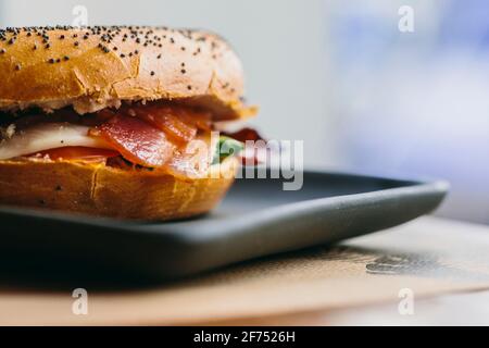 Sandwich au bagel appétissant avec du bacon et du poulet servi sur l'assiette sur la table dans le café Banque D'Images
