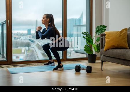 Femme brune mince en combinaison verte en position de squat Banque D'Images