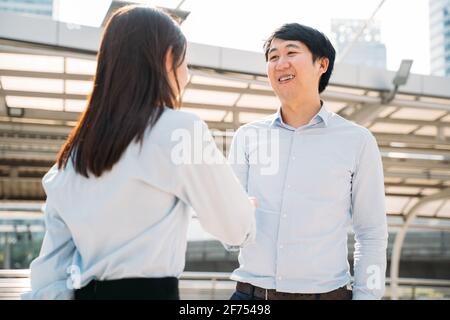 Portrait d'un jeune homme d'affaires asiatique souriant qui se tremble entre les mains une jeune femme employée à l'extérieur du bureau après avoir été sélectionnée pour tâche Banque D'Images