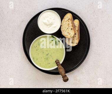 Soupe à la crème de brocoli servie avec de la crème et du pain frais sur fond de béton léger. Concept de nourriture végétarienne saine. Banque D'Images