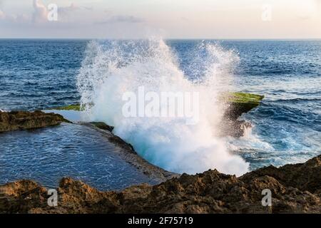 Vague se brisant contre la falaise à Devil's Tear, sur la côte de Nusa Lembongan, Bali, Indonésie. Piscine d'eau au sommet de la falaise en premier plan. Banque D'Images