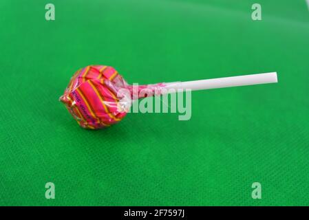 Délicieux bonbon rond, lollipop rose blanc sur baguette en plastique blanc situé sur fond de tissu vert. Banque D'Images