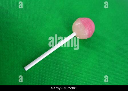 Délicieux bonbon rond, lollipop rose blanc sur baguette en plastique blanc situé sur fond de tissu vert. Banque D'Images