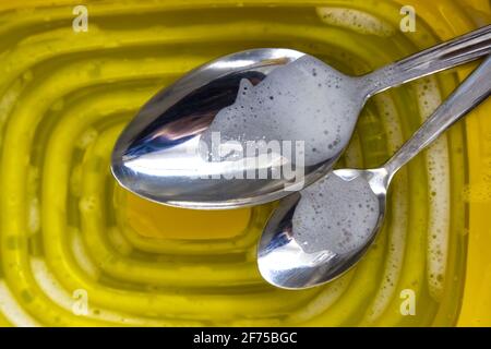 Macro photo de deux cuillères dans la phase de lavage sur couvercle en plastique jaune. Banque D'Images