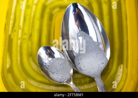Macro photo de deux cuillères dans la phase de lavage sur couvercle en plastique jaune. Banque D'Images