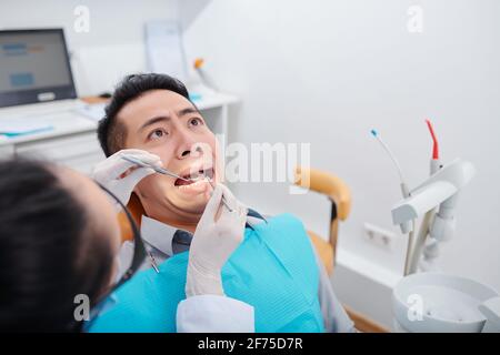 Un jeune homme asiatique effrayé fait un visage drôle quand il obtient son dents traitées en clinique Banque D'Images