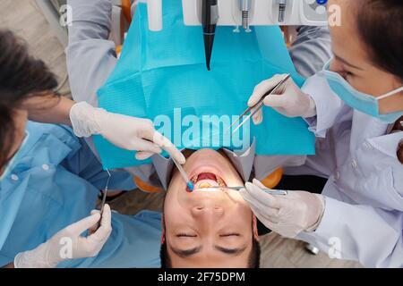 Patient assis dans une chaise dentaire avec sa bouche largement ouverte lorsque le dentiste vérifie les dents et recherche la cavité, les maladies des gencives et la plaque dentaire Banque D'Images