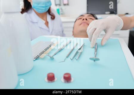 Dentiste en gants de silicone prenant des outils métalliques du plateau quand examen des dents des patients Banque D'Images